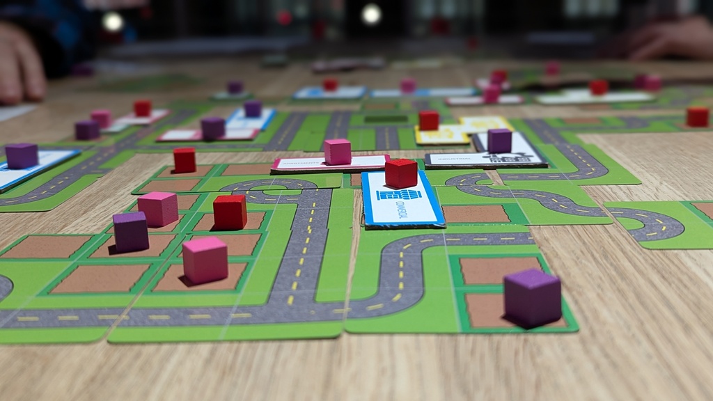 upclose view of the game in during a session. The cards are laid out on a table with cubes on properties and building tiles on the cards.